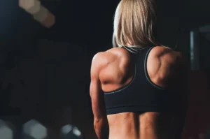 A focused athlete in a black tank top showing defined back muscles, embodying the results of following effective online fitness advice