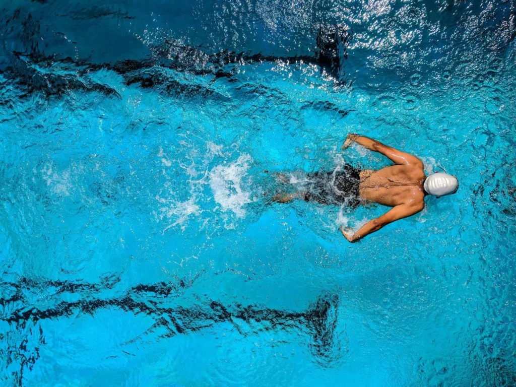 An overhead view of a swimmer in a pool, with arms mid-stroke, training intensively, a depiction of the discipline and preparation offered by a training plan platform.