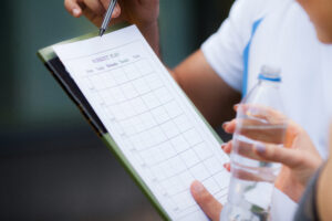 Close-up of a person holding a workout plan clipboard and a water bottle, highlighting the importance of planning and hydration for smart workouts.