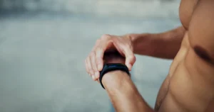 A fit man checking his fitness tracker on his wrist, emphasizing the importance of monitoring exercise time to manage time for fitness effectively.