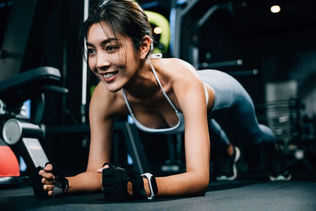 Smiling woman performing a plank exercise as part of core training in a gym.