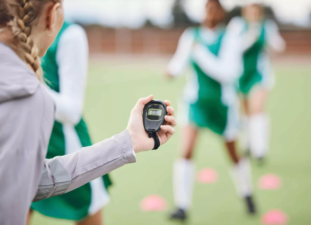 Coach holding a timer while athletes perform drills, tracking Efficiency Factor (EF) to optimize training performance.