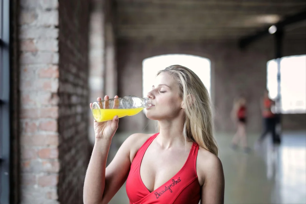 A woman in a red sports bra drinking an orange hydration drink after exercise, emphasizing the importance of nutrition and hydration.