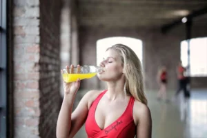 A woman in a red sports bra drinking an orange hydration drink after exercise, emphasizing the importance of nutrition and hydration.