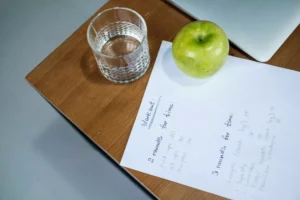 Workout plan on paper next to a glass of water and an apple, symbolizing race strategy and tactics preparation.
