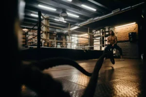 A muscular man performing battle rope exercises in a gym, emphasizing fueling systems for muscle contractions during high-intensity training.
